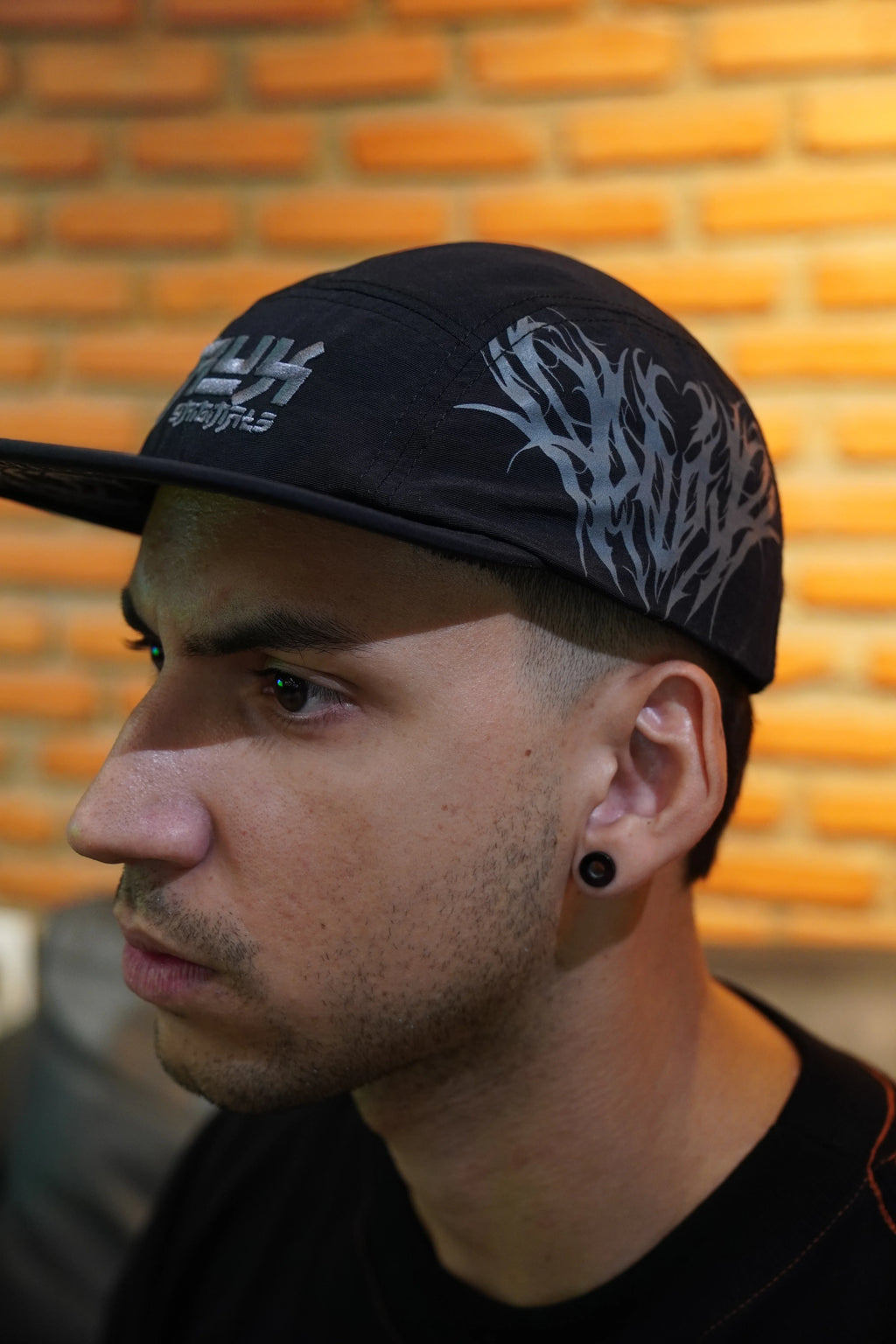 Model wearing a black five panel cap with silver gothic graphics side view