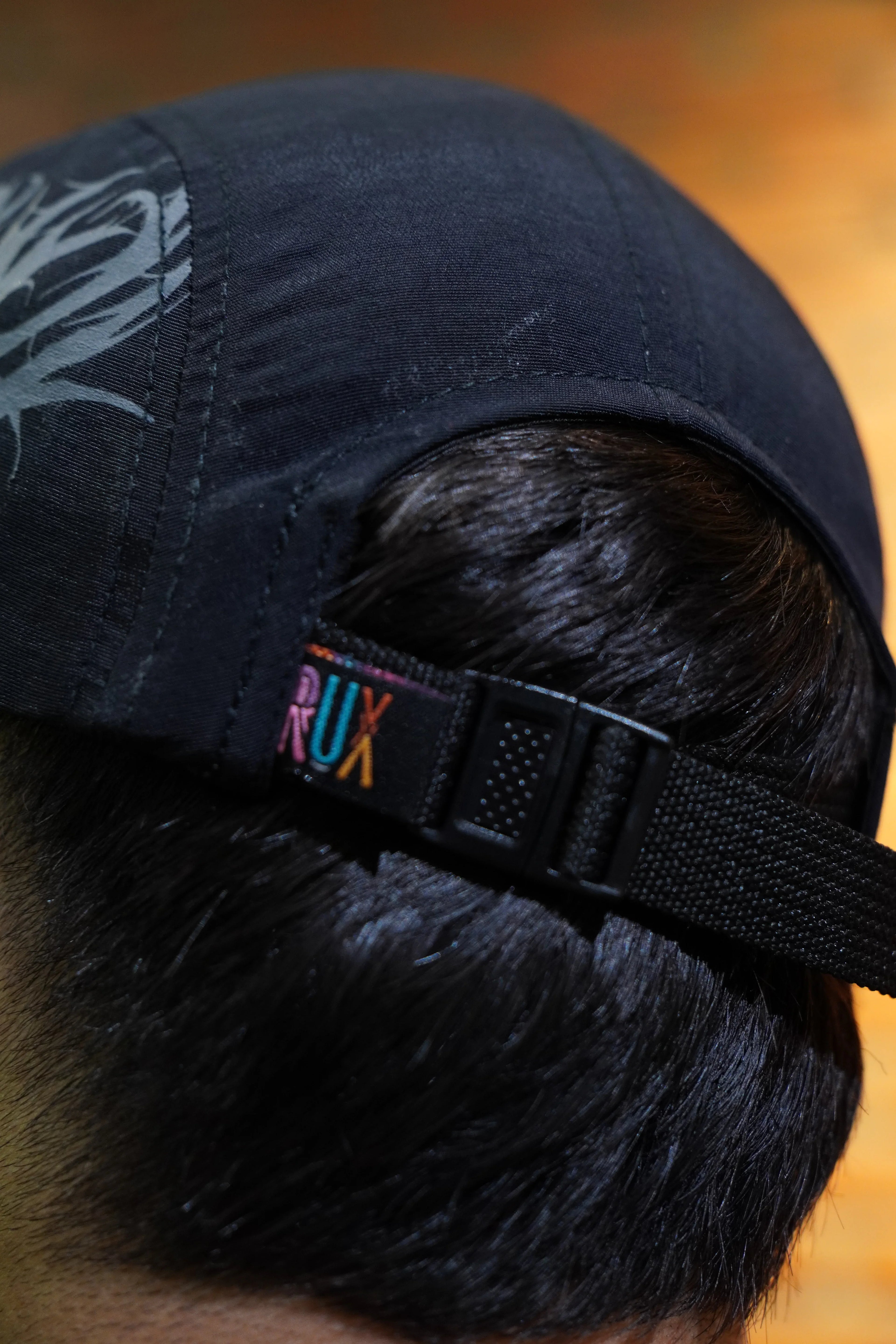 Close-up of a model wearing a black five-panel cap with embroidery and adjustable strap