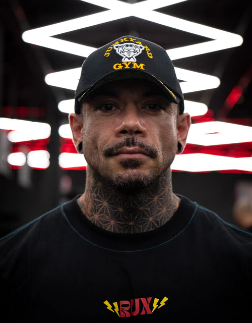 Model wearing black Junkyard Gym cap and RUX t-shirt with geometric neck tattoo indoors