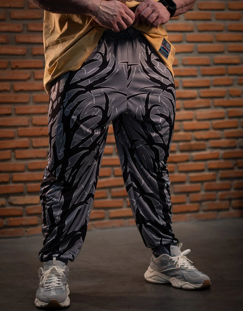 Model wearing black and gray patterned balloon pants with sneakers against a brick wall