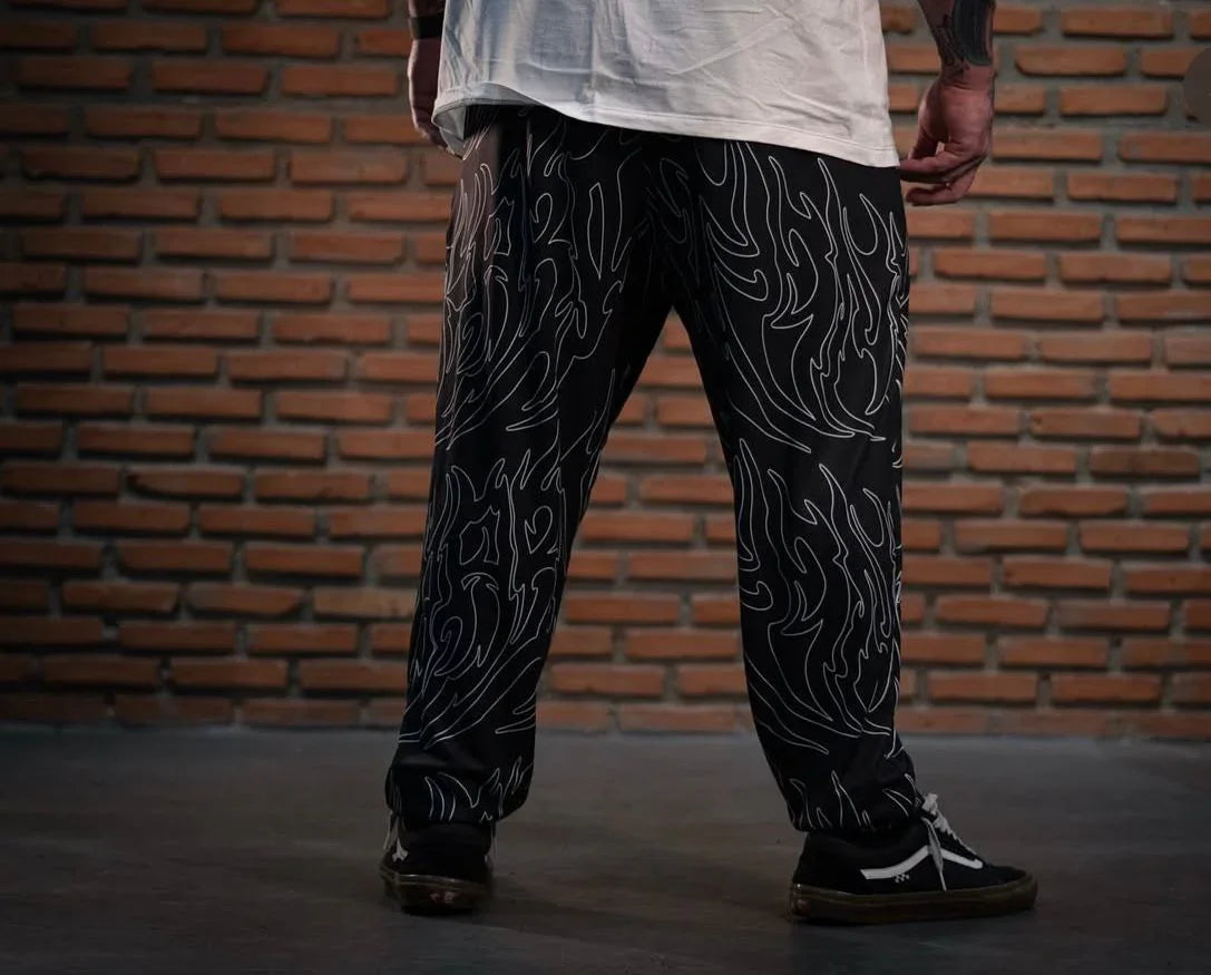 Model wearing black graphic pants with a white abstract flame pattern, standing indoors