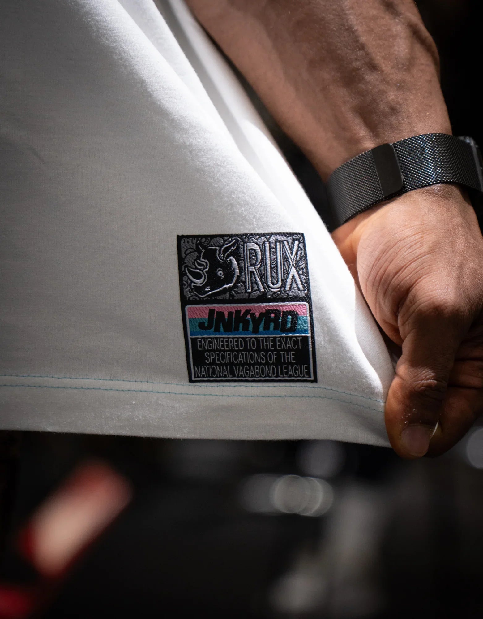 Model wearing pants showing white fabric detail with black logo patch and hand visible.