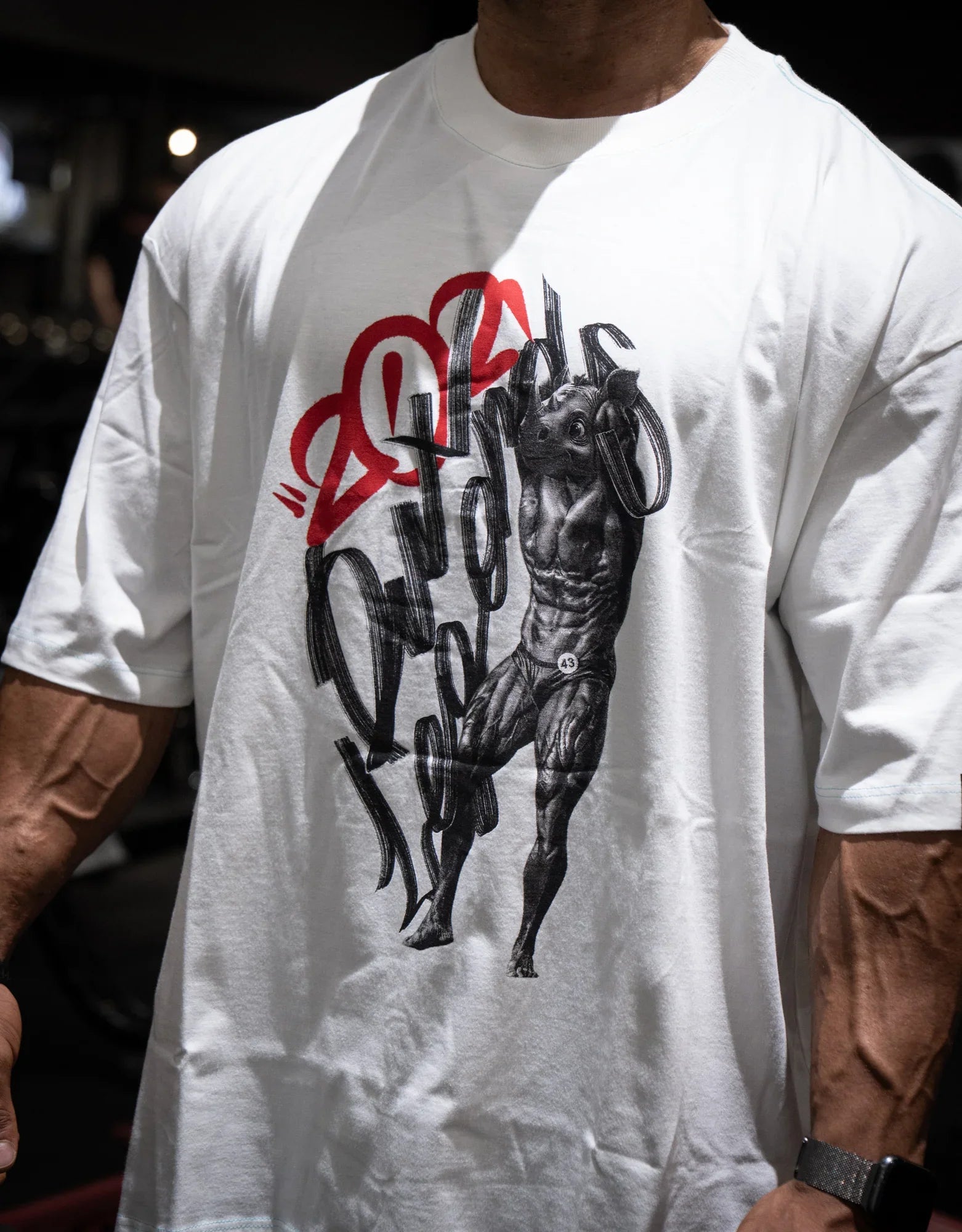 Model wearing oversized white graphic t-shirt with black and red muscle figure print