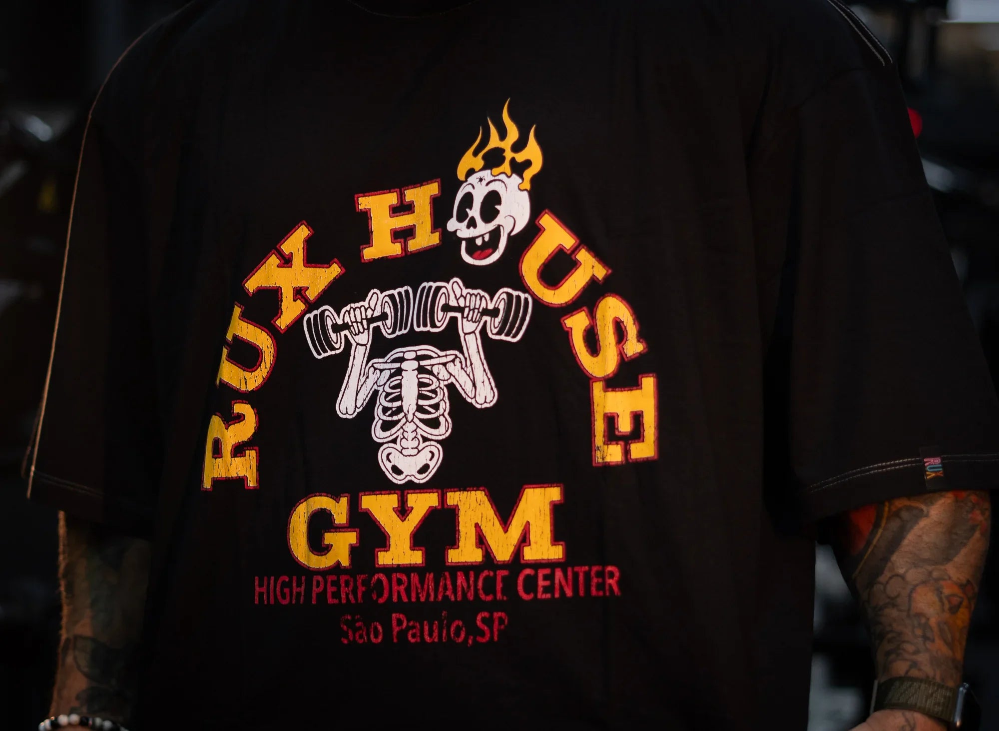 Model wearing black t-shirt with Rux House Gym skeleton weightlifting graphic.