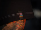 Model wearing black pants with colorful RUX logo tag and visible leg tattoo