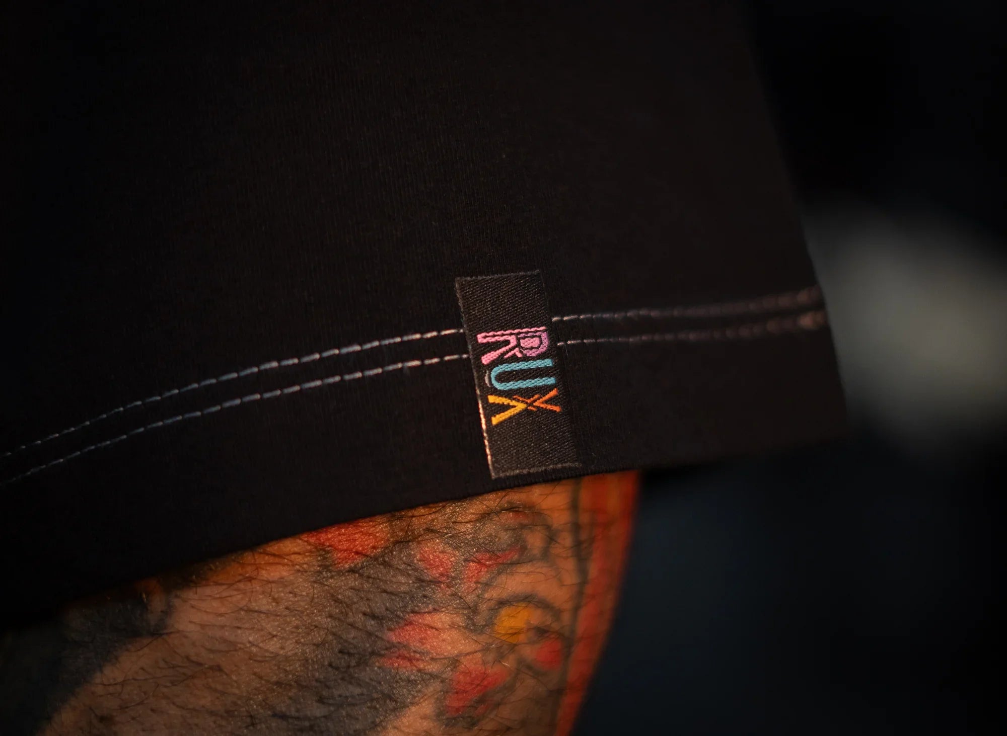 Model wearing black pants with colorful RUX logo tag and visible leg tattoo
