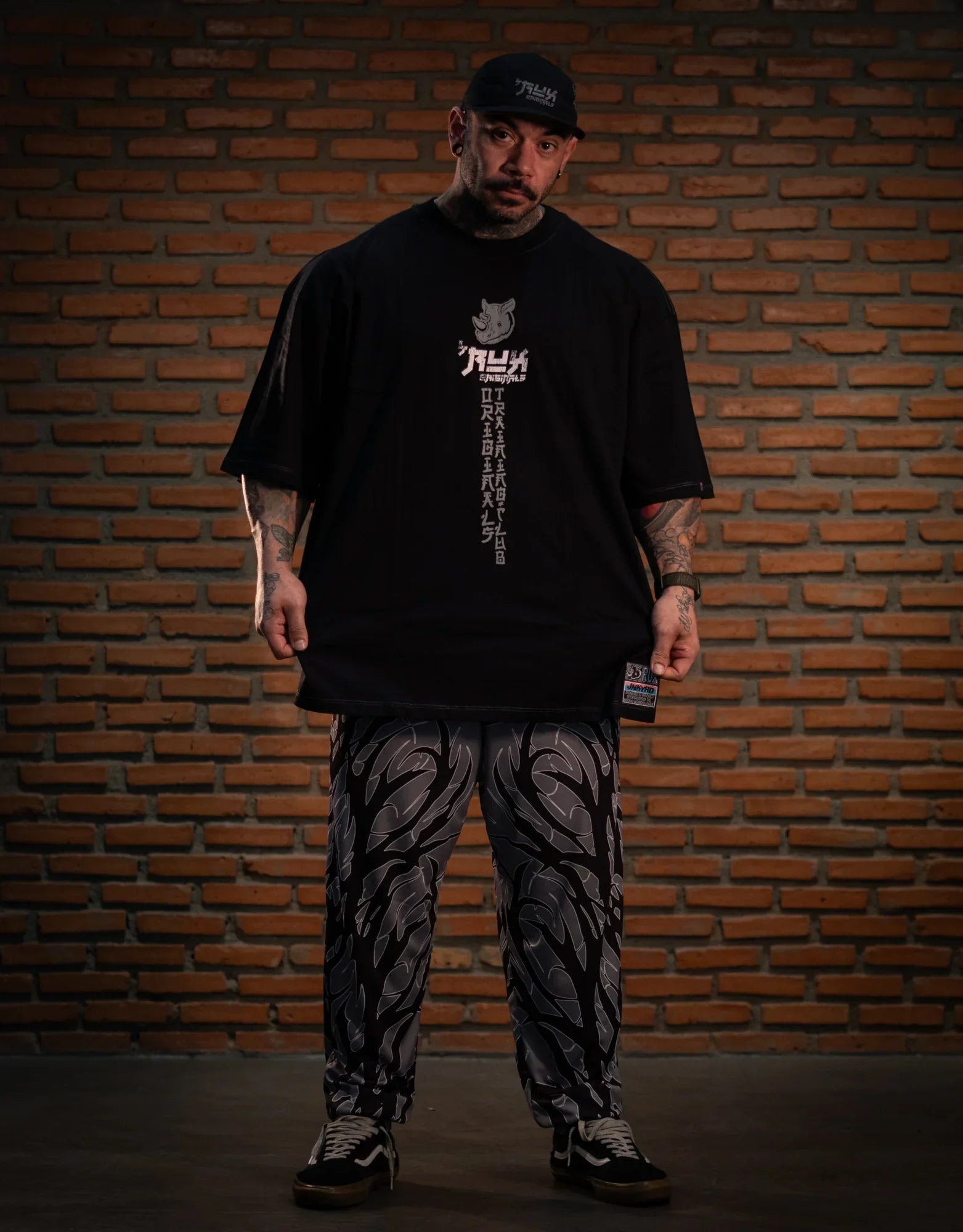 Model wearing graphic black shirt and patterned black pants in front of brick wall