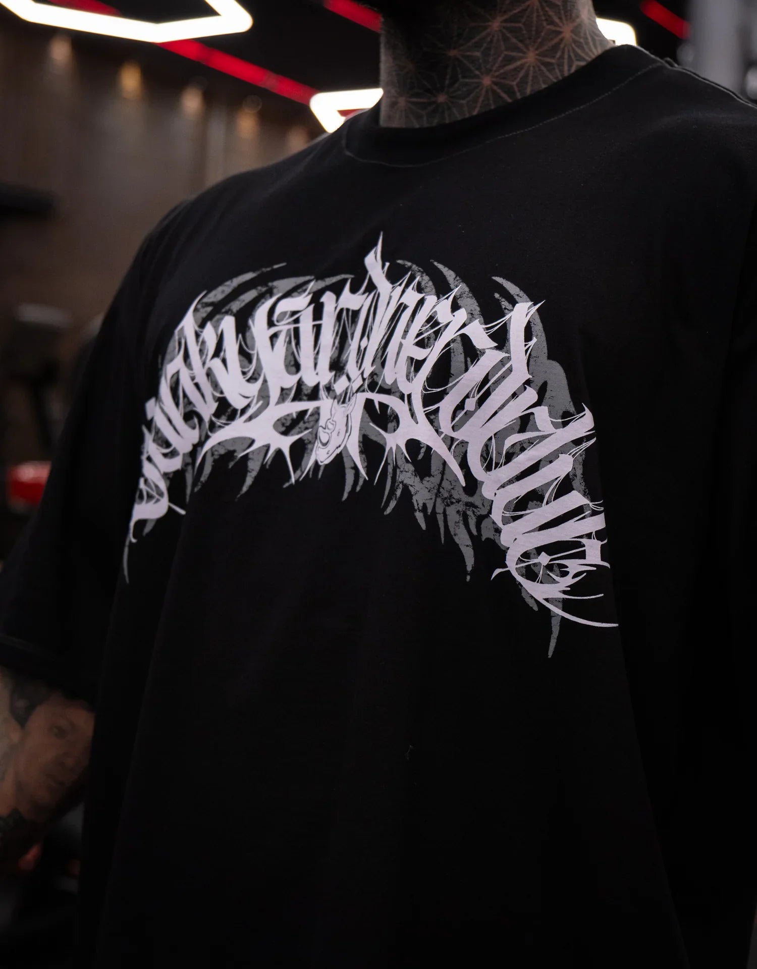 Model wearing black graphic t-shirt with bold white logo design in an indoor setting