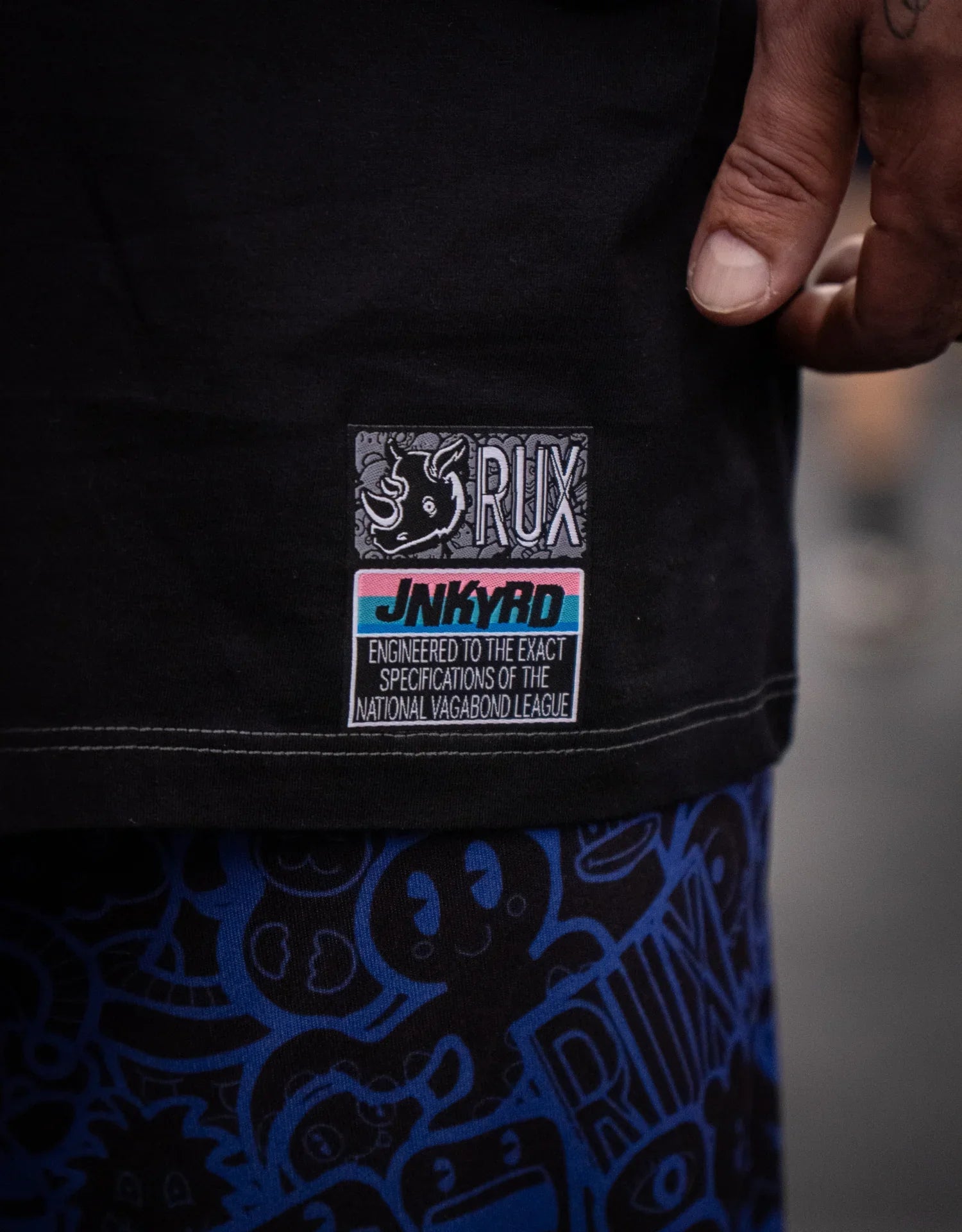 Model wearing blue graphic print pants, hand visible, close-up on pants and shirt tag