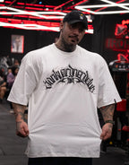 Model wearing oversized white graphic t-shirt and black cap in gym setting