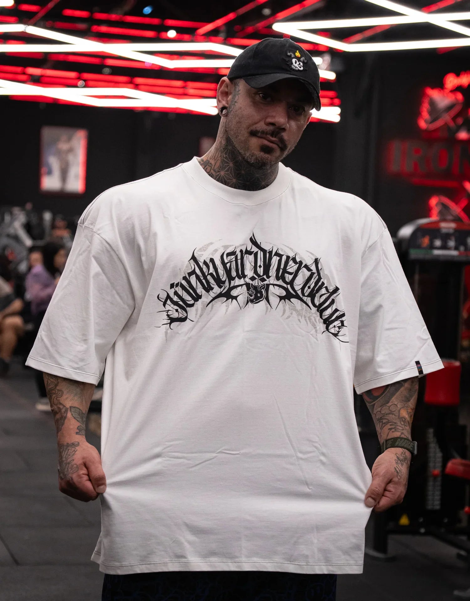 Model wearing oversized white graphic t-shirt and black cap in gym setting