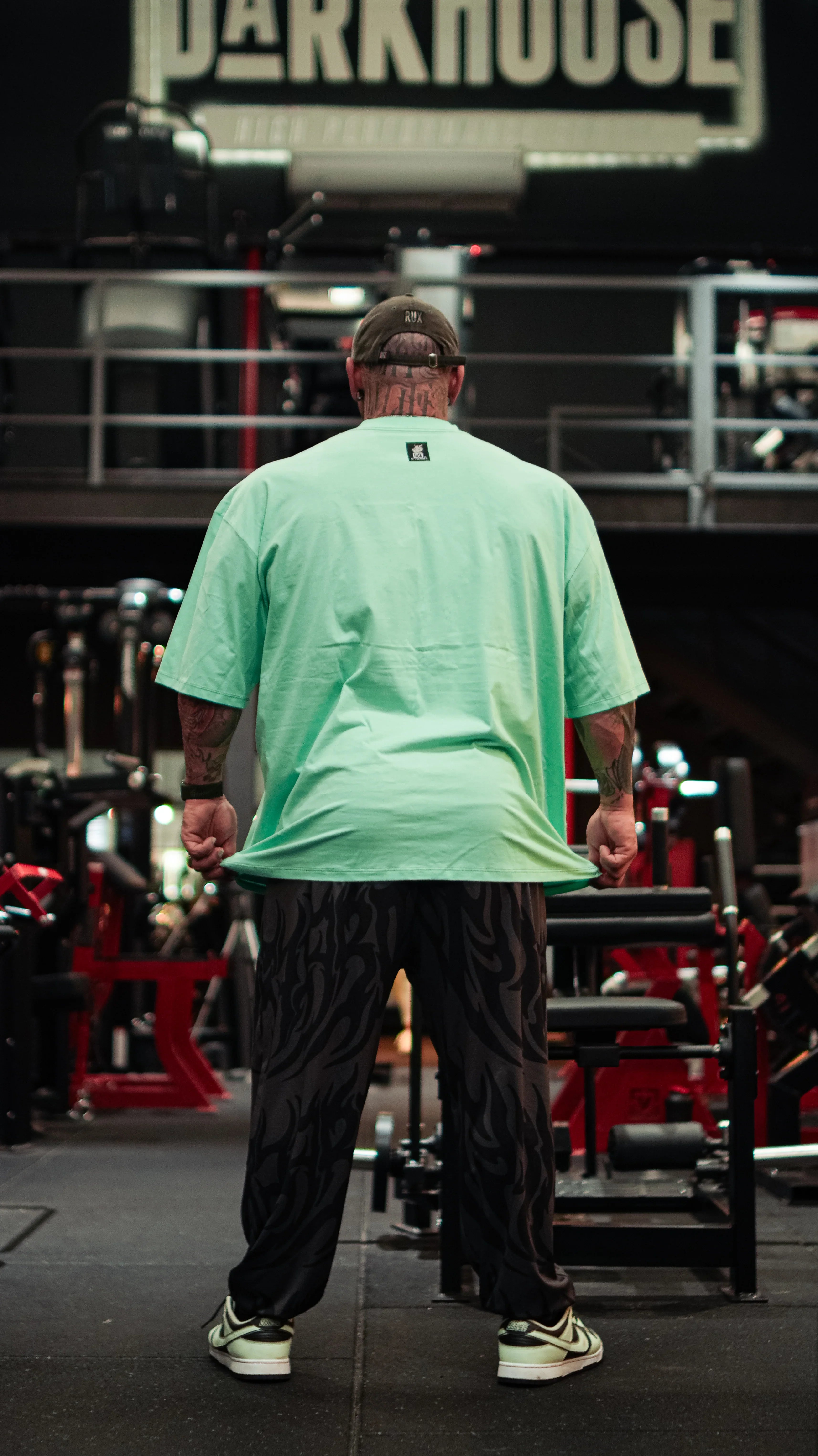Model wearing patterned gym pants in a fitness center, viewed from behind