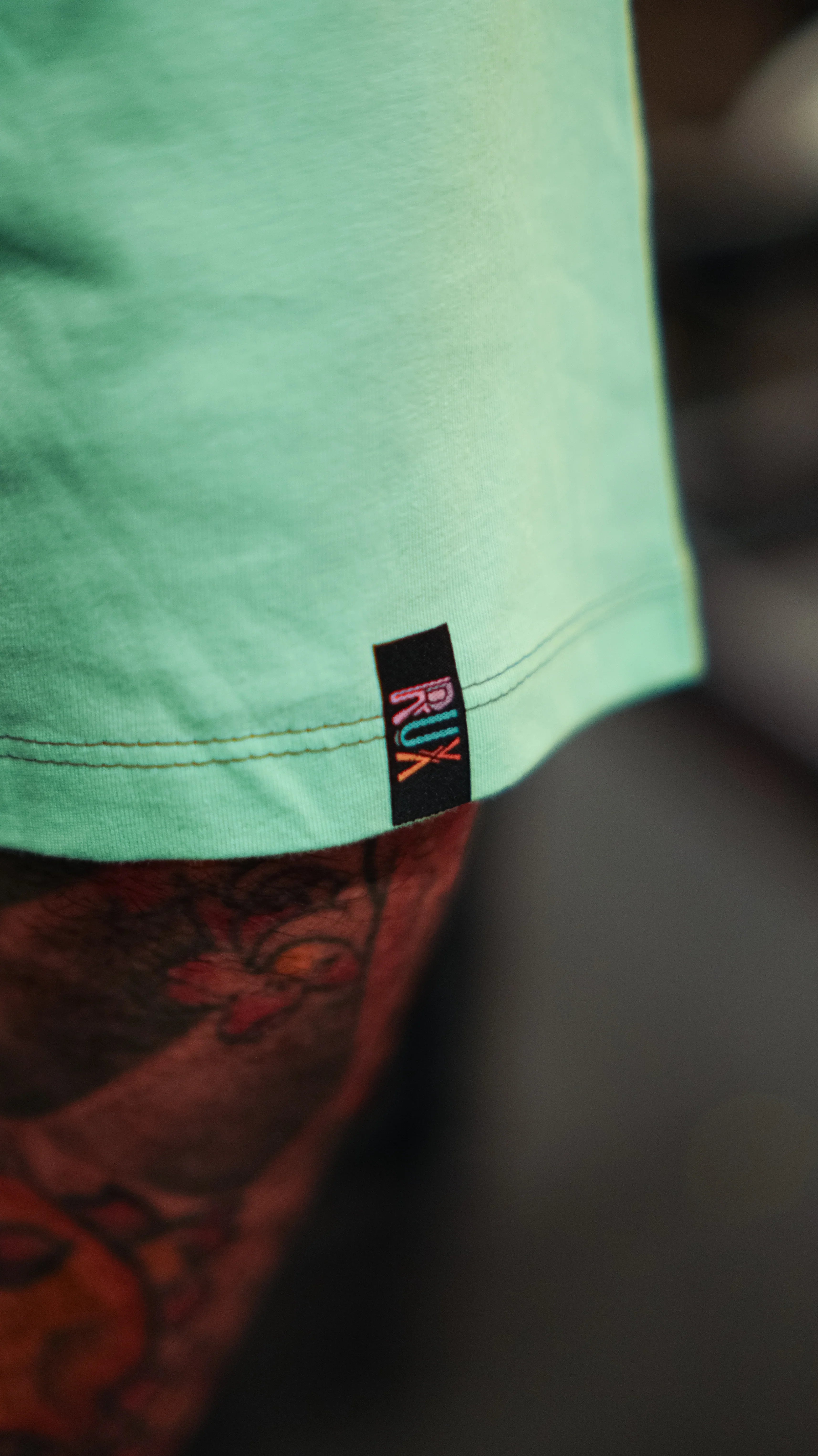 Model wearing pants with a visible tattooed leg and mint green shirt close-up