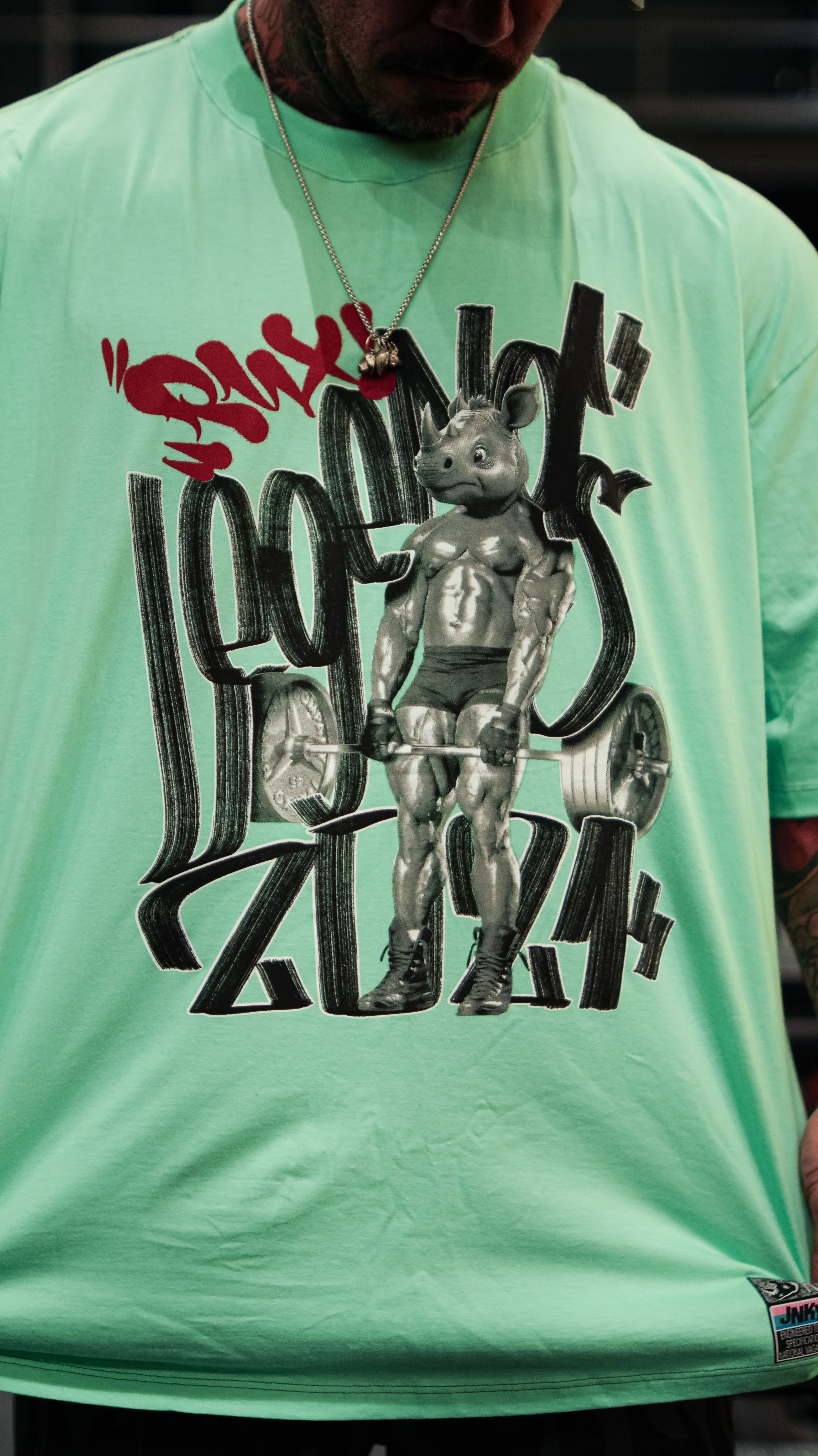 Model wearing pants, mint green graphic t-shirt featuring a muscular cartoon rhino.