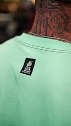 Model wearing turquoise shirt with visible neck tattoos and a logo tag on the back