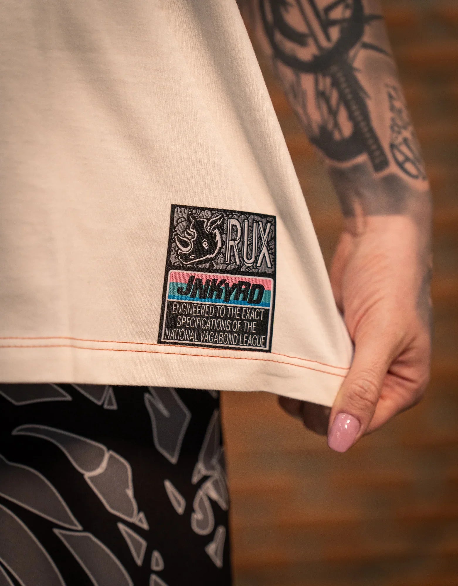Model wearing patterned workout pants with a close-up of a tattooed hand and shirt hem patch