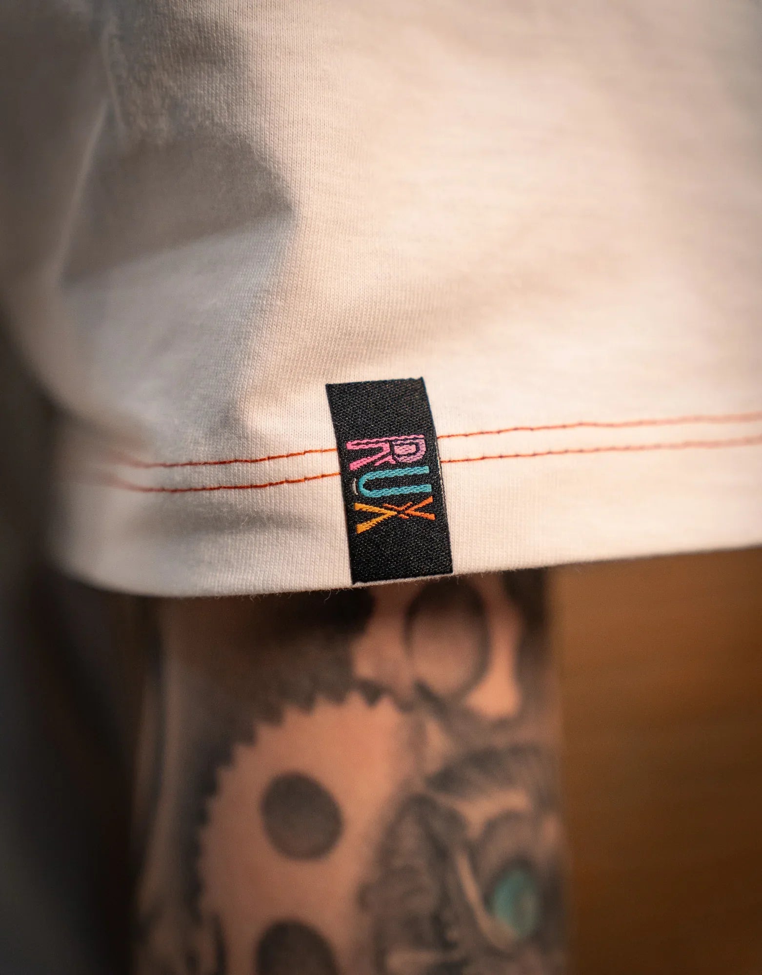 Model wearing pants with visible logo tag, tattooed leg, and orange stitching detail