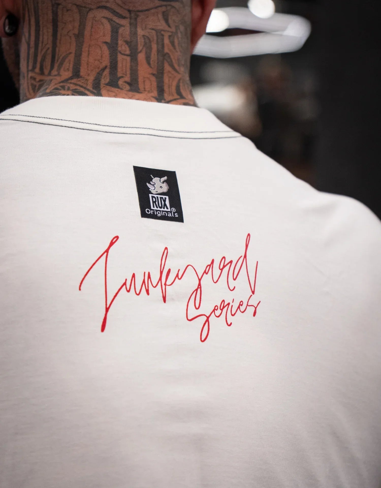 Close up of model wearing white t-shirt with 'Junkyard Series' red text and neck tattoo visible