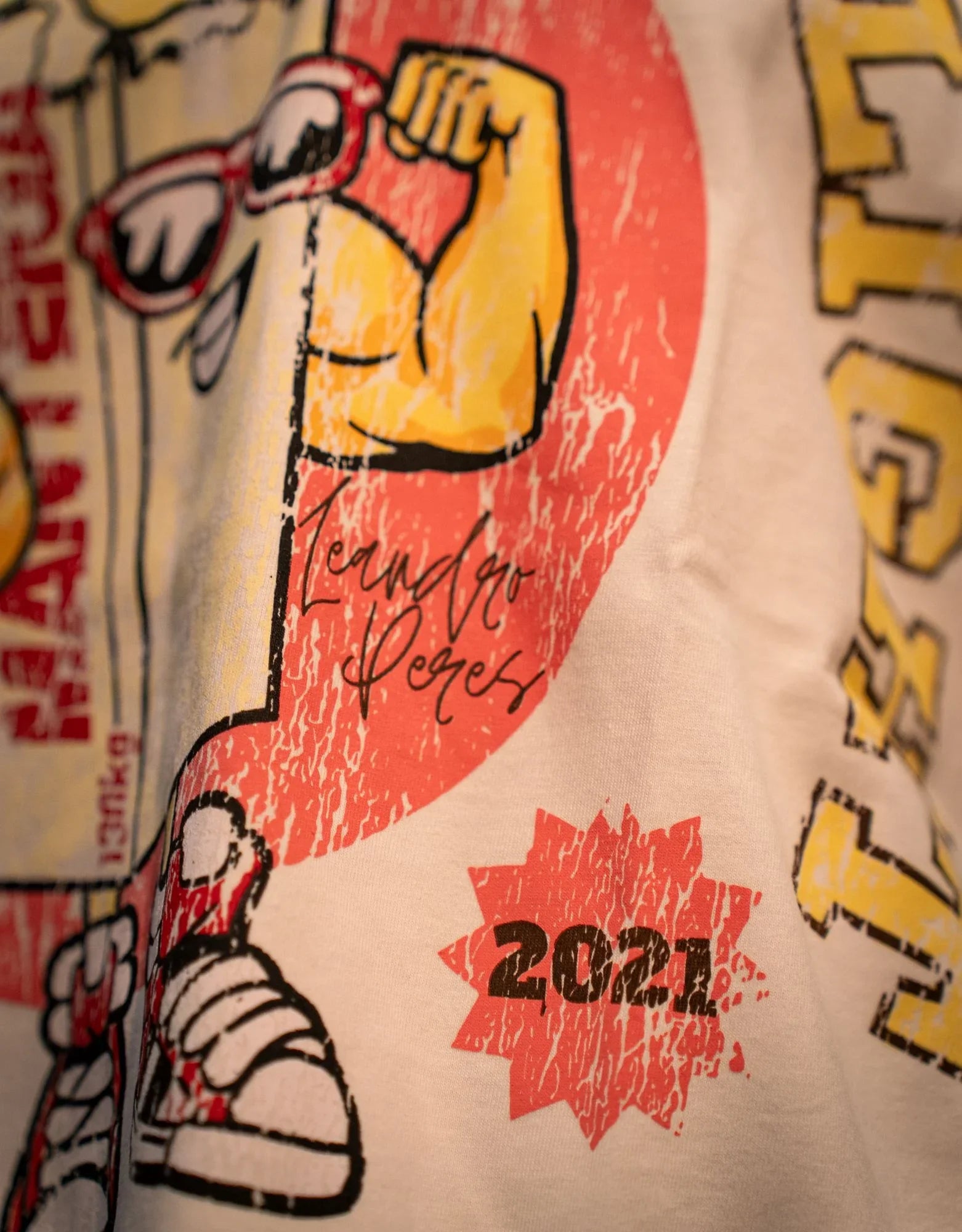 Close-up of cartoon graphic on pants featuring flexed arm, sneakers, and '2021' text.