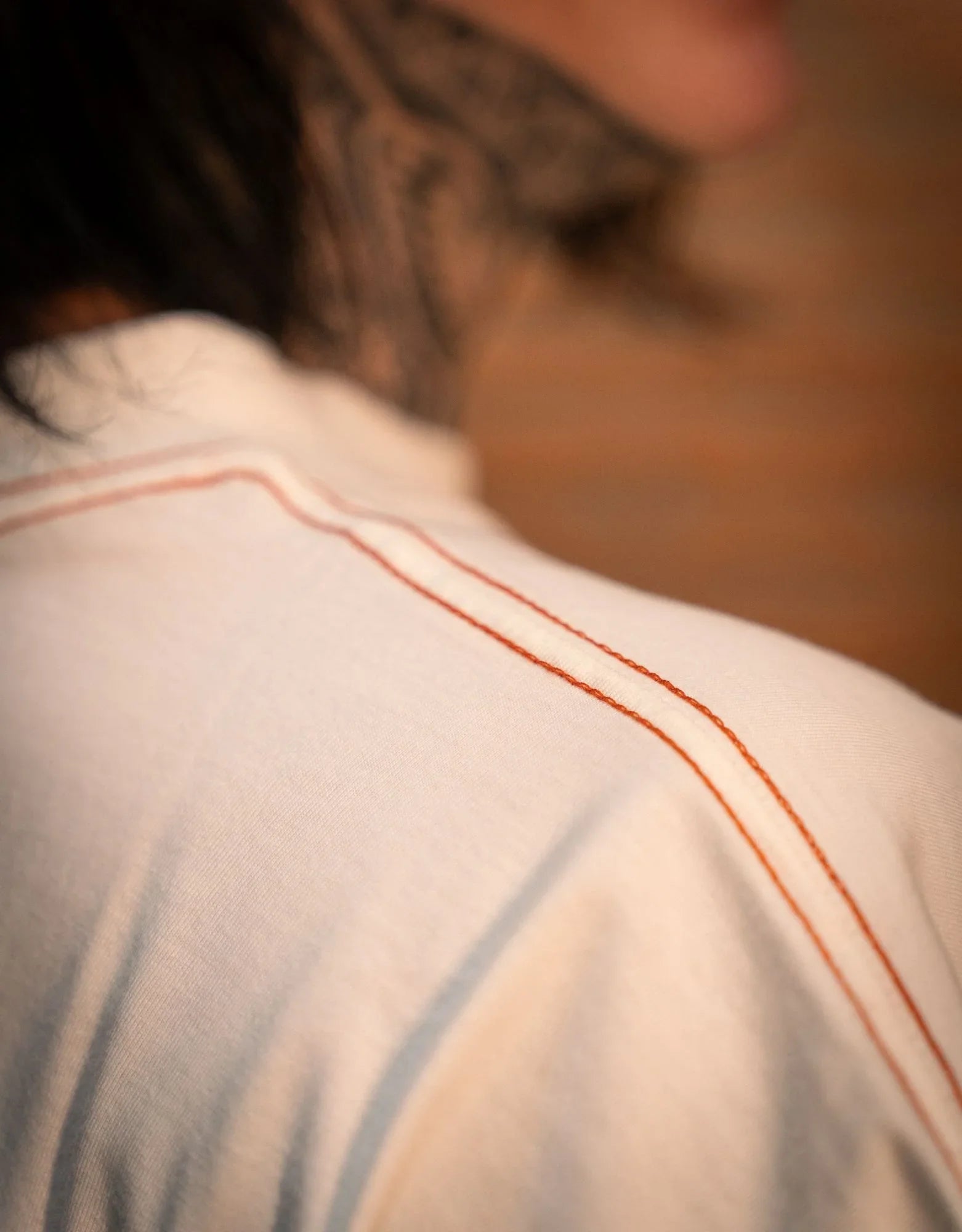 Close-up of white shirt with orange seam detail on shoulder, person with neck tattoo