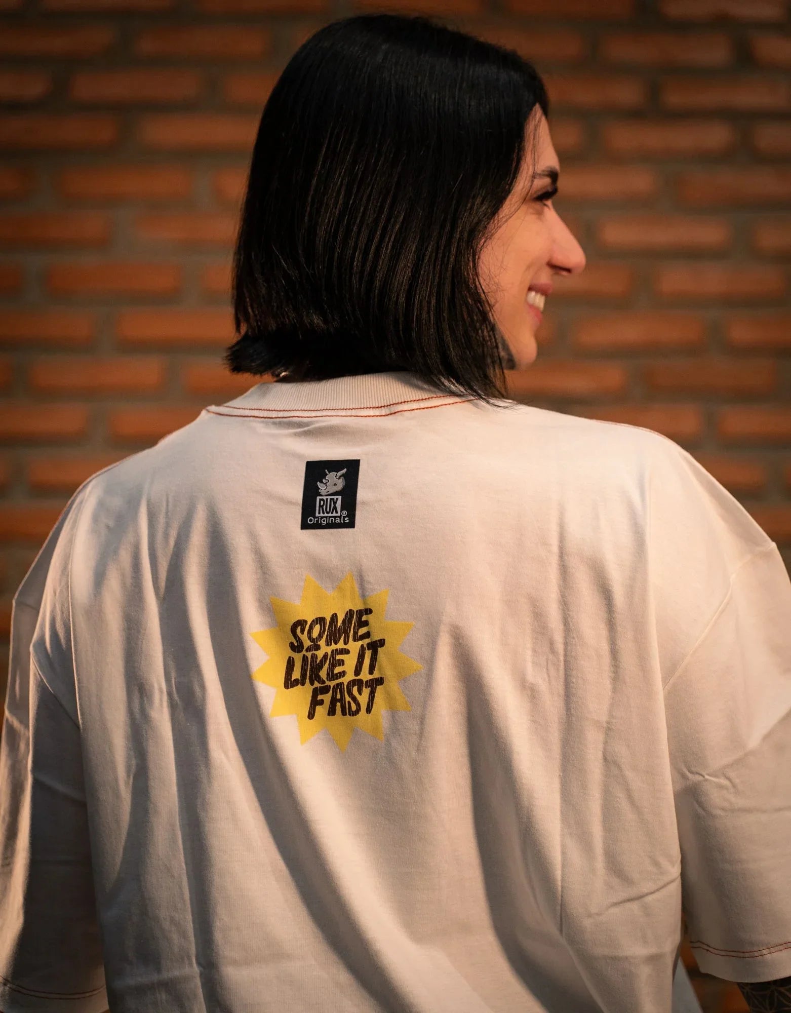 Model showing graphic t-shirt back with 'Some Like It Fast' print and short black hair